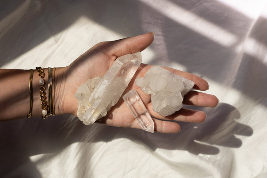 Womens hand holding a large clear quartz crystal point, small clear quartz crystal point, and a clear quartz crystal cluster.